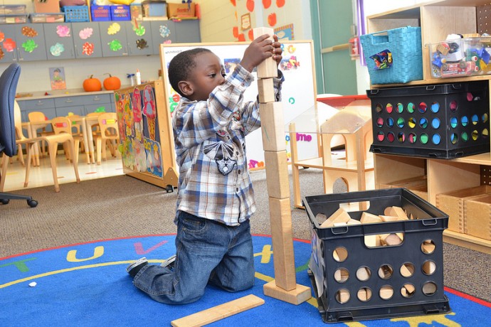 A Head Start student at Next Door Foundation reaches for the sky with his block tower. (Photo by Sue Vliet)
