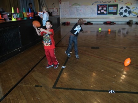 First-grade students practice throwing a football during gym class. (Photo by Raina J. Johnson)