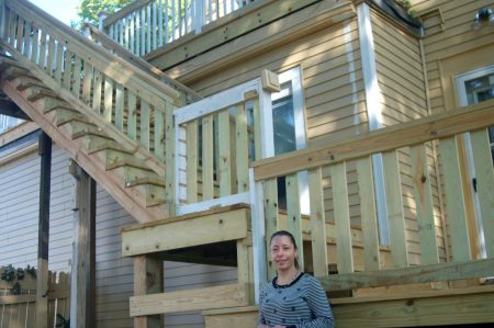 Maria Alvarado stands at the base of the staircase and upper deck built with funds provided by the Department of Neighborhood Service's Code Loan Program. (Photo by Edgar Mendez)