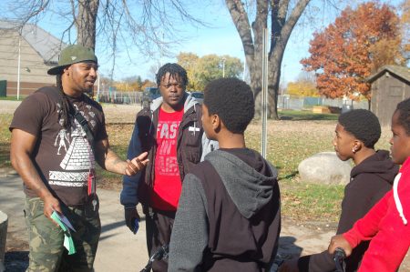 Vaun Mayes (left) talks to several teens riding bikes in the neighborhood about joining the Sherman Park Youth Stipend Program. Volunteer mentor Derrick Madlock (second from left) looks on. (Photo by Andrea Waxman)