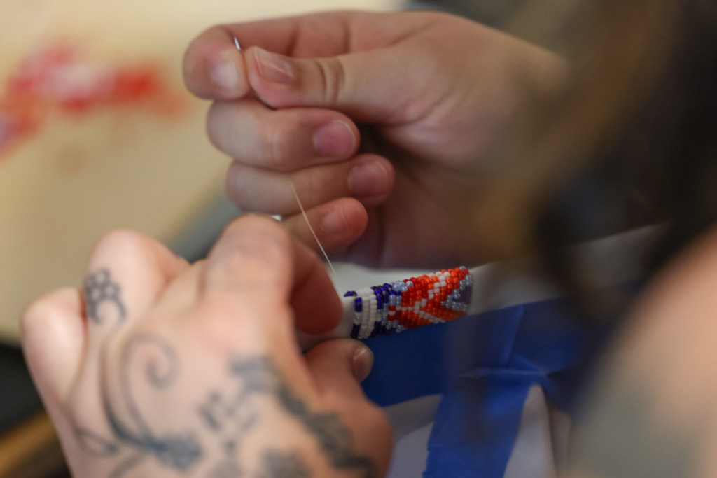 A person's hands sew red, white, and blue beads onto blue fabric
