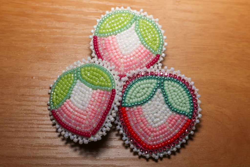 Three pink, white, and green beaded strawberry-shaped designs rest on a wooden surface nearby.