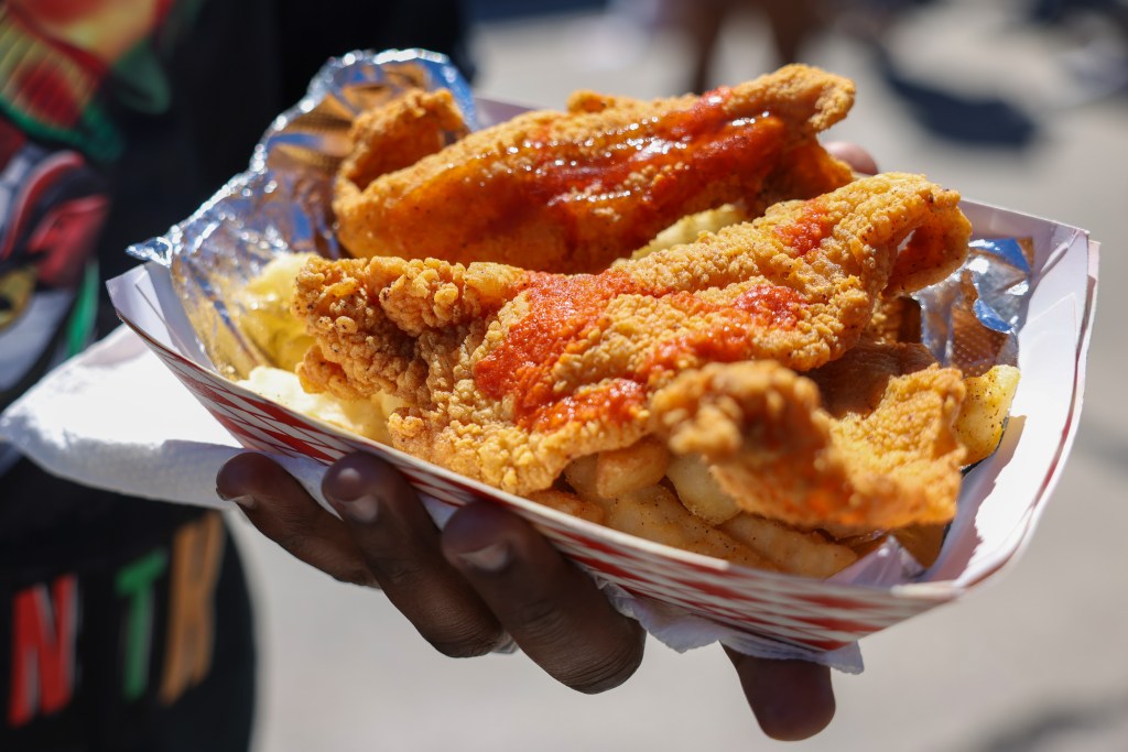 A person holds a container of fried fish and French fries during the 55th Juneteenth Jubilee Parade on Friday, June 19, 2026 in Milwaukee. (Photo by Jonathan Aguilar / Milwaukee Neighborhood News Service)