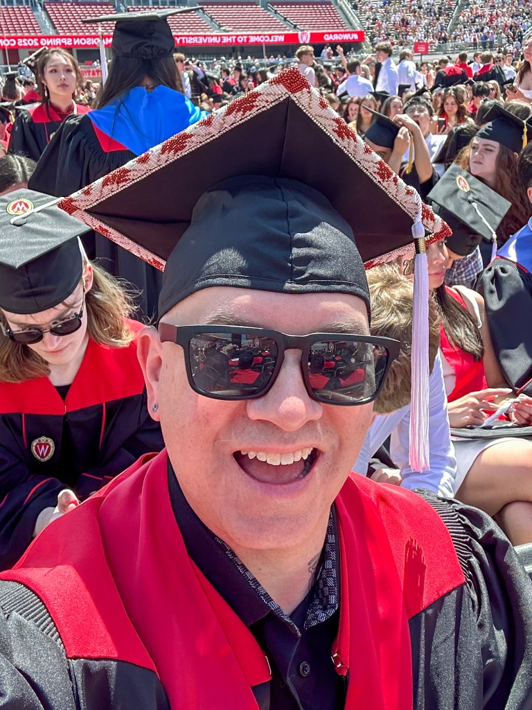A person wears a cap among graduates in a stadium.